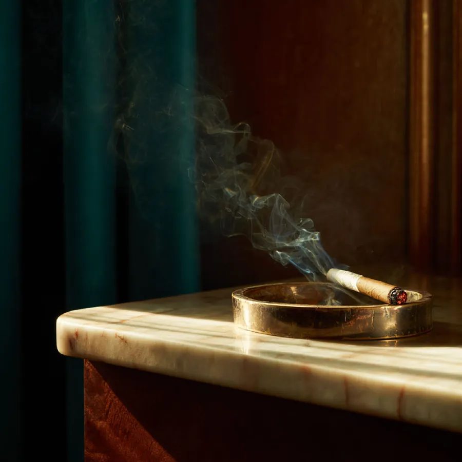 A cigar in a brass ashtray on marble