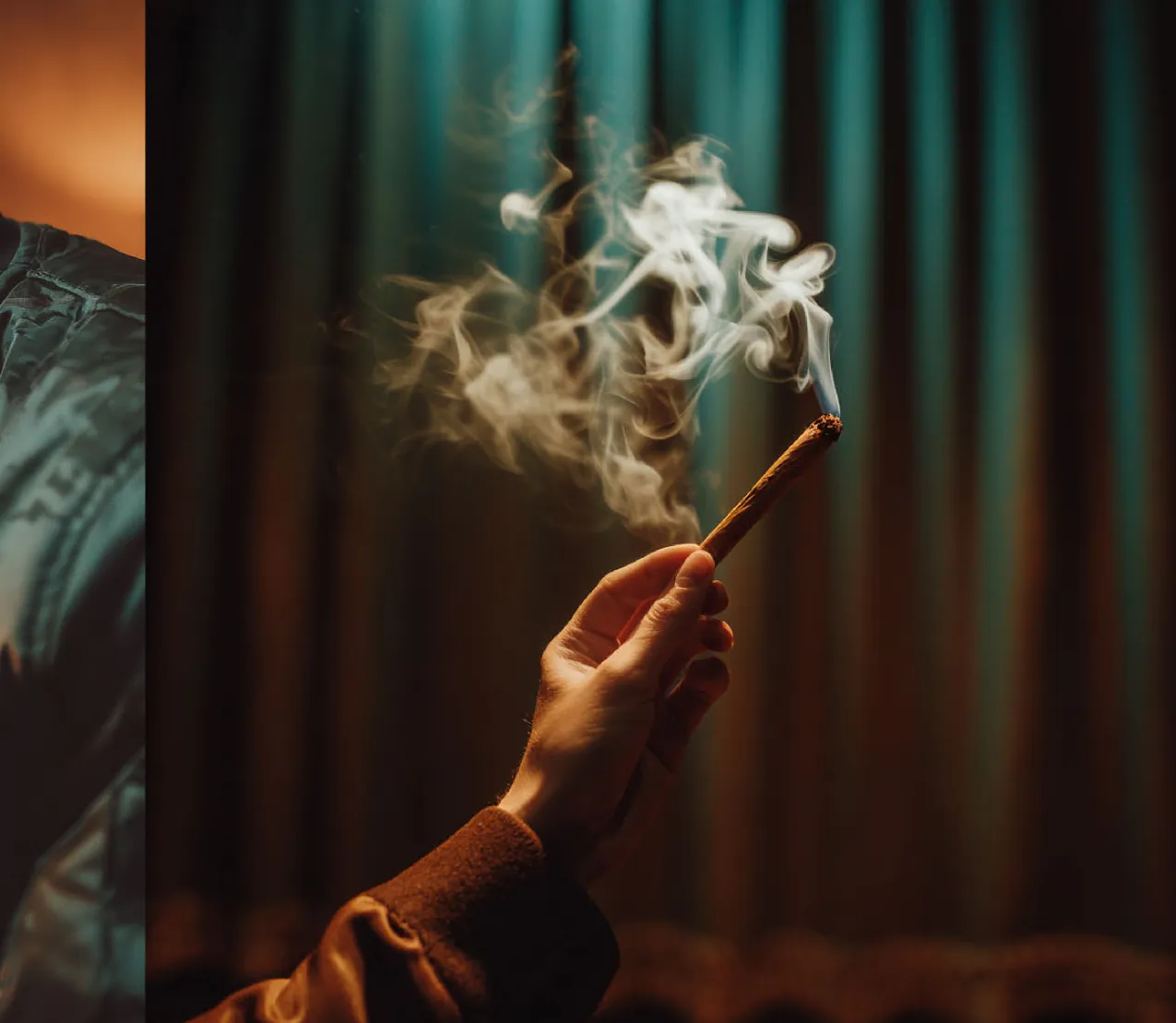 A hand holding a lit wrap, smoke curling against a teal curtain